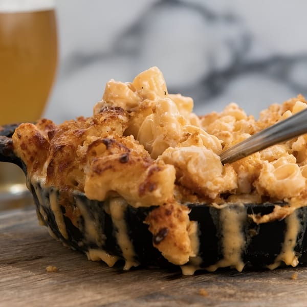 Close-up of baked mac and cheese in a cast iron skillet with a beer in the background.