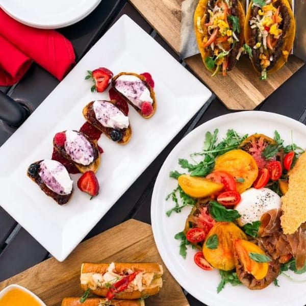 Overhead view of various dishes including bruschetta, tacos, a tomato salad, and lobster rolls.