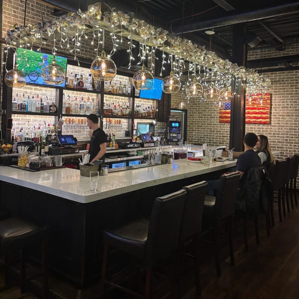 Uncommon Grill's bar with a bartender, two patrons, and festive lights hanging above.
