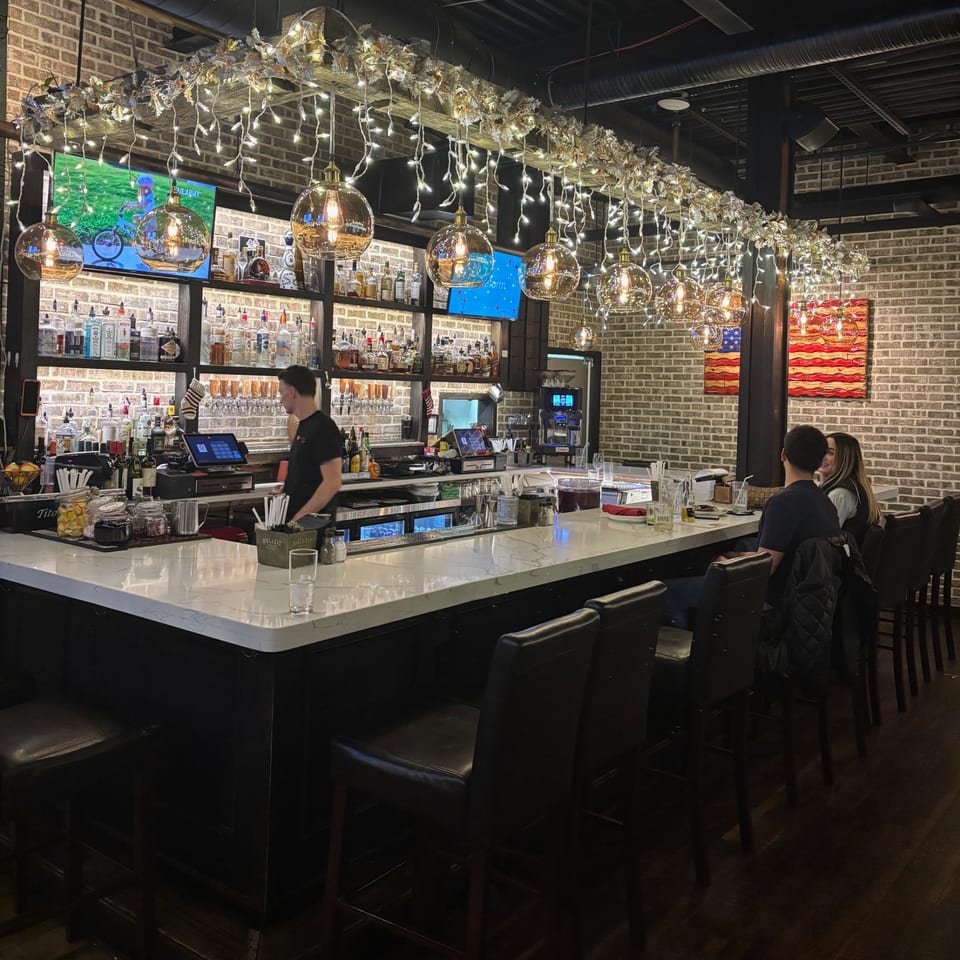 Uncommon Grill's bar with a bartender, two patrons, and festive lights hanging above.