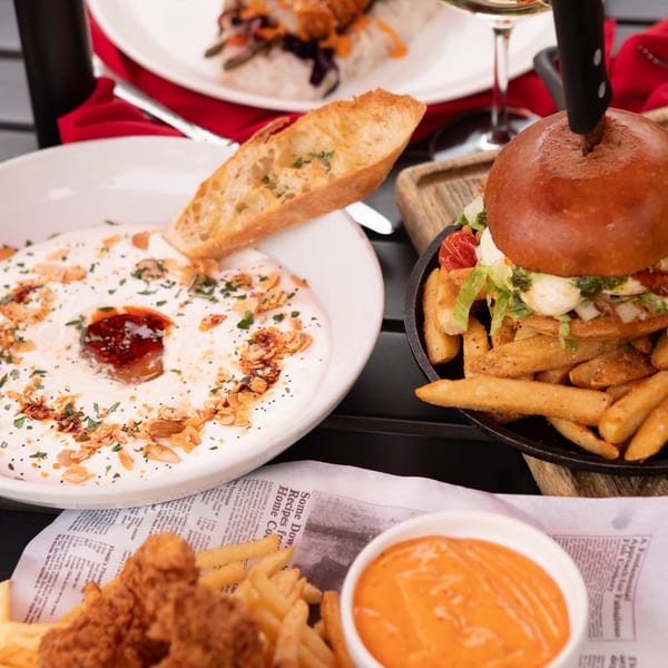 A table spread with a burger and fries, a bowl of dip with bread, and fried chicken.