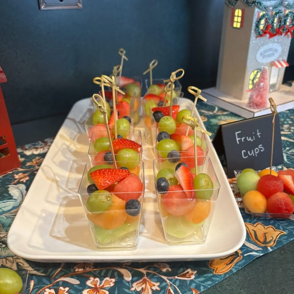 A white tray holds rows of fruit cups with strawberries, grapes, blueberries, and melon.