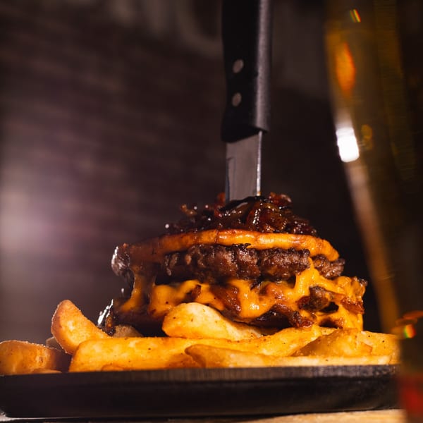 A double cheeseburger with caramelized onions and a knife through it, served with fries.