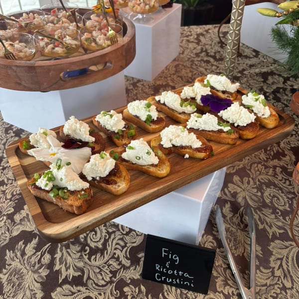 Fig and Ricotta Crostini with edible flowers and shrimp ceviche in glasses on a buffet.