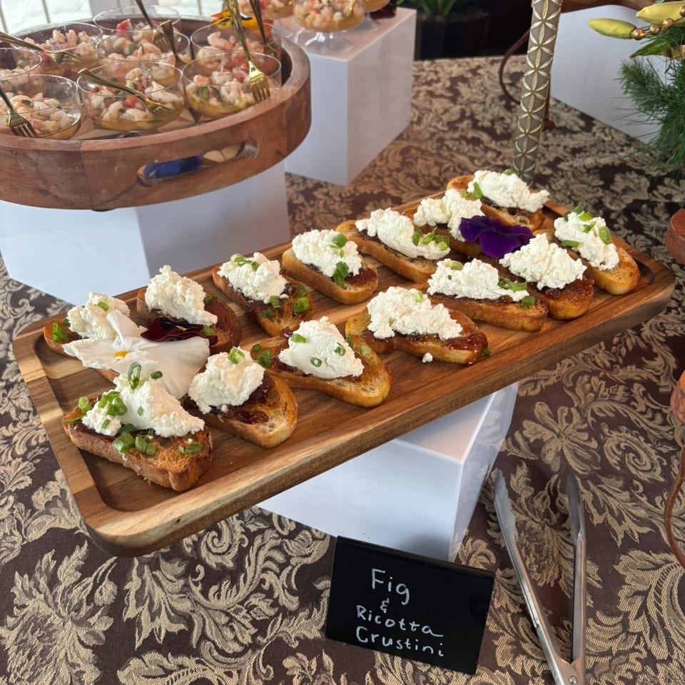 Fig and Ricotta Crostini with edible flowers and shrimp ceviche in glasses on a buffet.