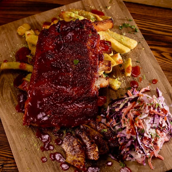 Uncommon Grill's BBQ ribs, golden fries, and coleslaw served on a rustic wooden board.