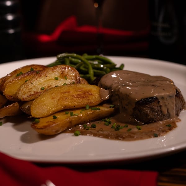Uncommon Grill's steak with creamy mushroom sauce, roasted potatoes, and green beans on a white plate.