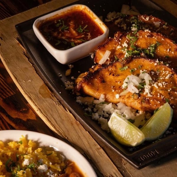 Three crispy tacos with cheese, onions, cilantro, and lime, served with a side of red sauce.