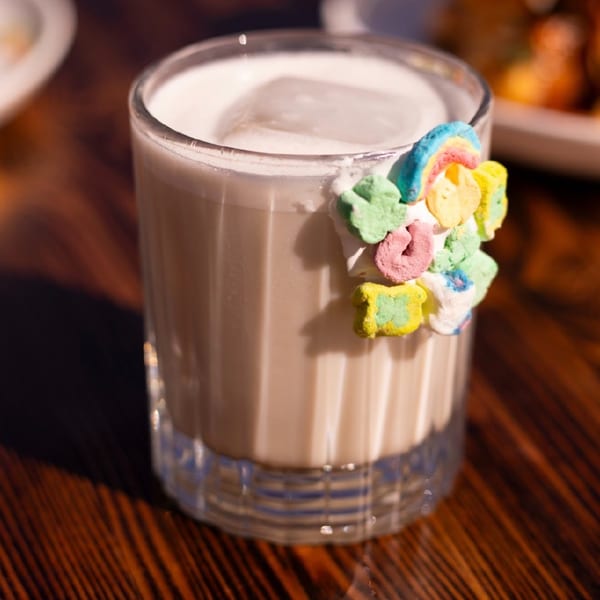 Creamy cocktail in a glass, garnished with colorful Lucky Charms marshmallows on a wooden table.