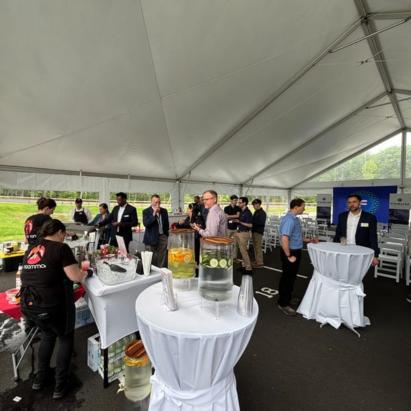 People mingling under a white tent with a bar, food, and drink dispensers at an outdoor event.
