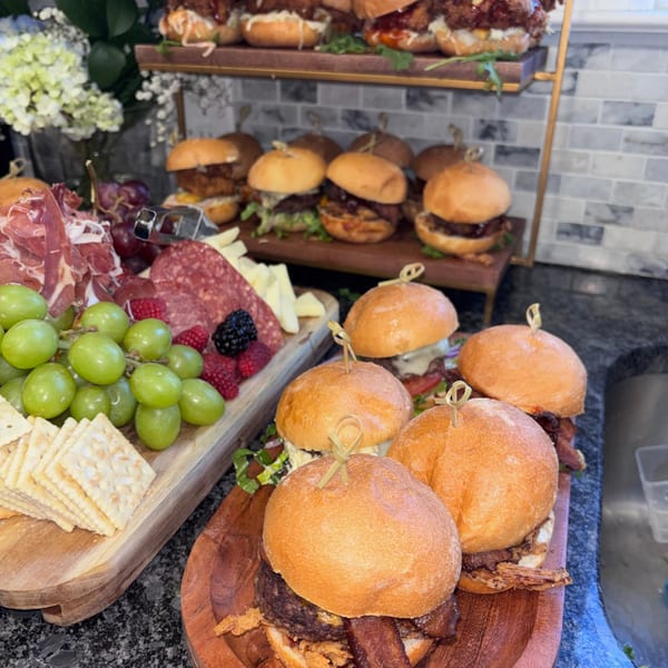 A charcuterie board with grapes, crackers, meats, and cheeses next to a tiered display of sliders.