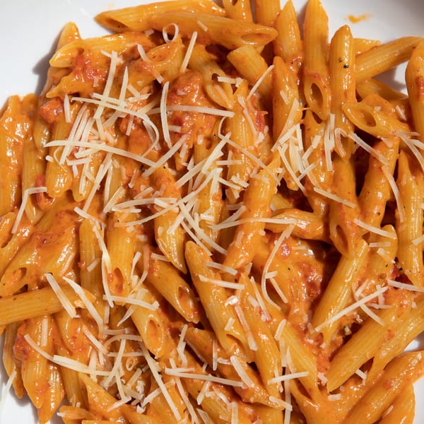 Penne pasta in a creamy orange sauce, topped with shredded white cheese in a white bowl.