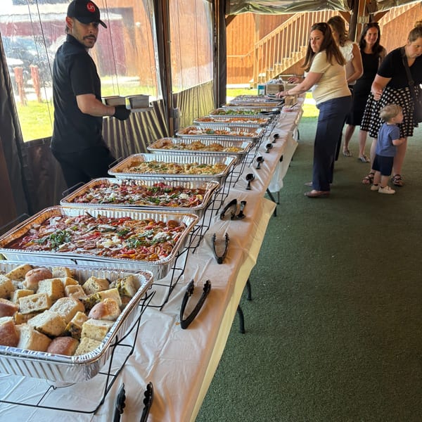 A buffet line with various hot dishes and bread, served by a staff member to guests.